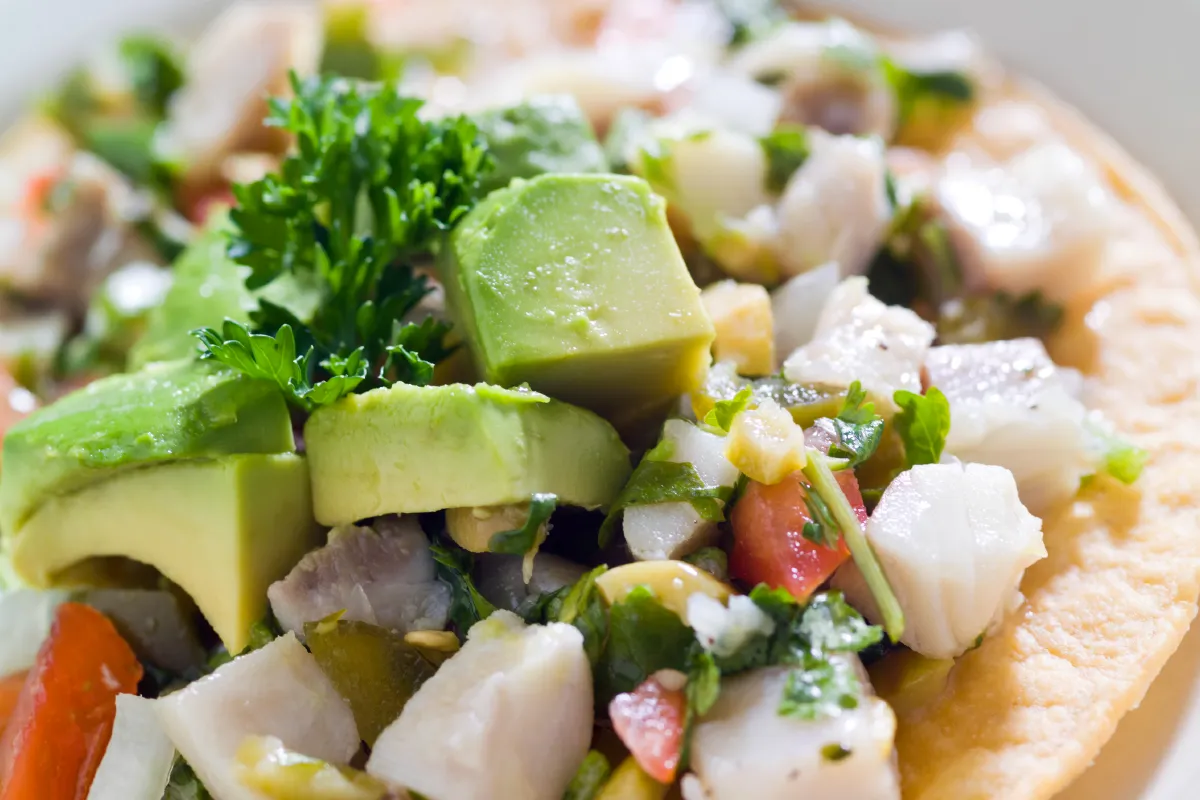 Close-up of a vibrant seafood ceviche with avocado cubes, cilantro, and diced tomatoes on a crispy tostada.