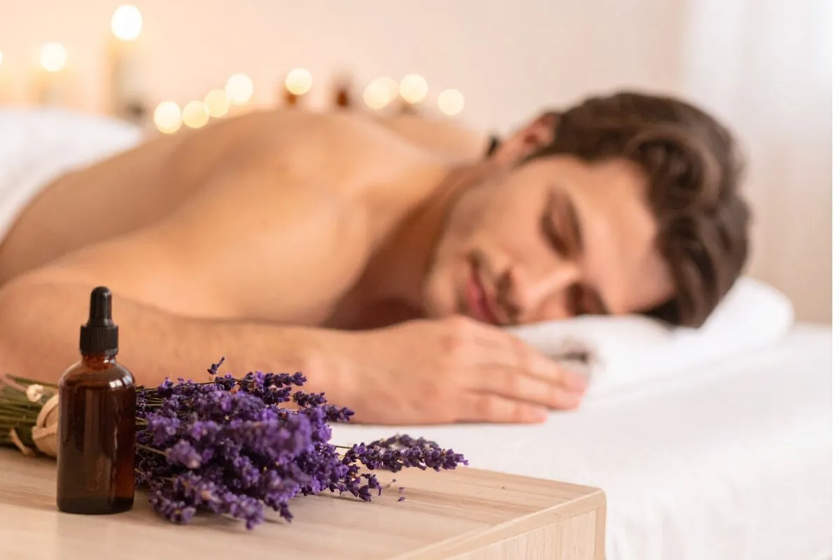 Man relaxing on a massage table with lavender and essential oil nearby, basking in a tranquil spa ambiance.