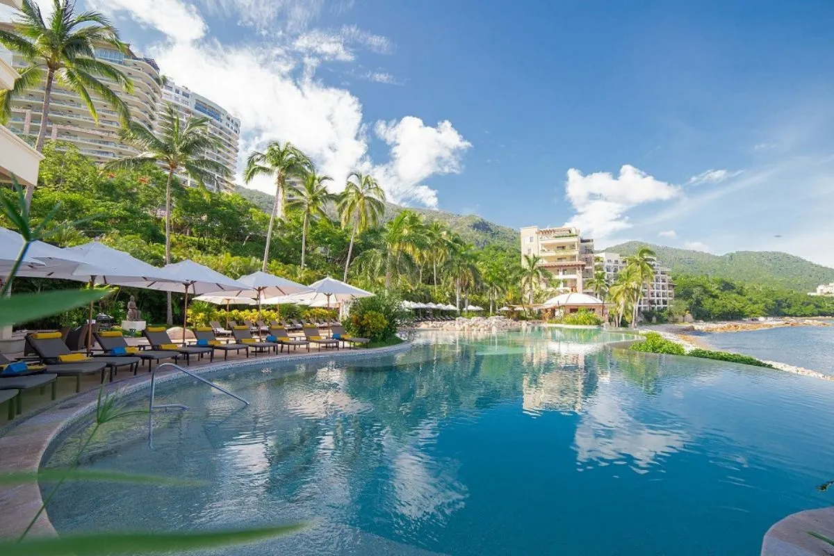 Infinity pool at a luxury beachfront resort in Cancun, surrounded by palm trees and sun loungers, with ocean view under a blue sky.