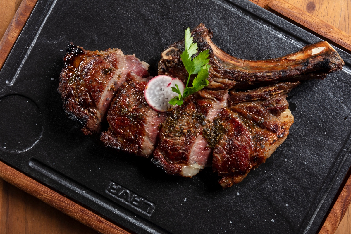 Garza Blanca Cabo gourmet bone-in ribeye, sliced medium-rare with charred crust, radish and parsley on a black cast-iron serving board.