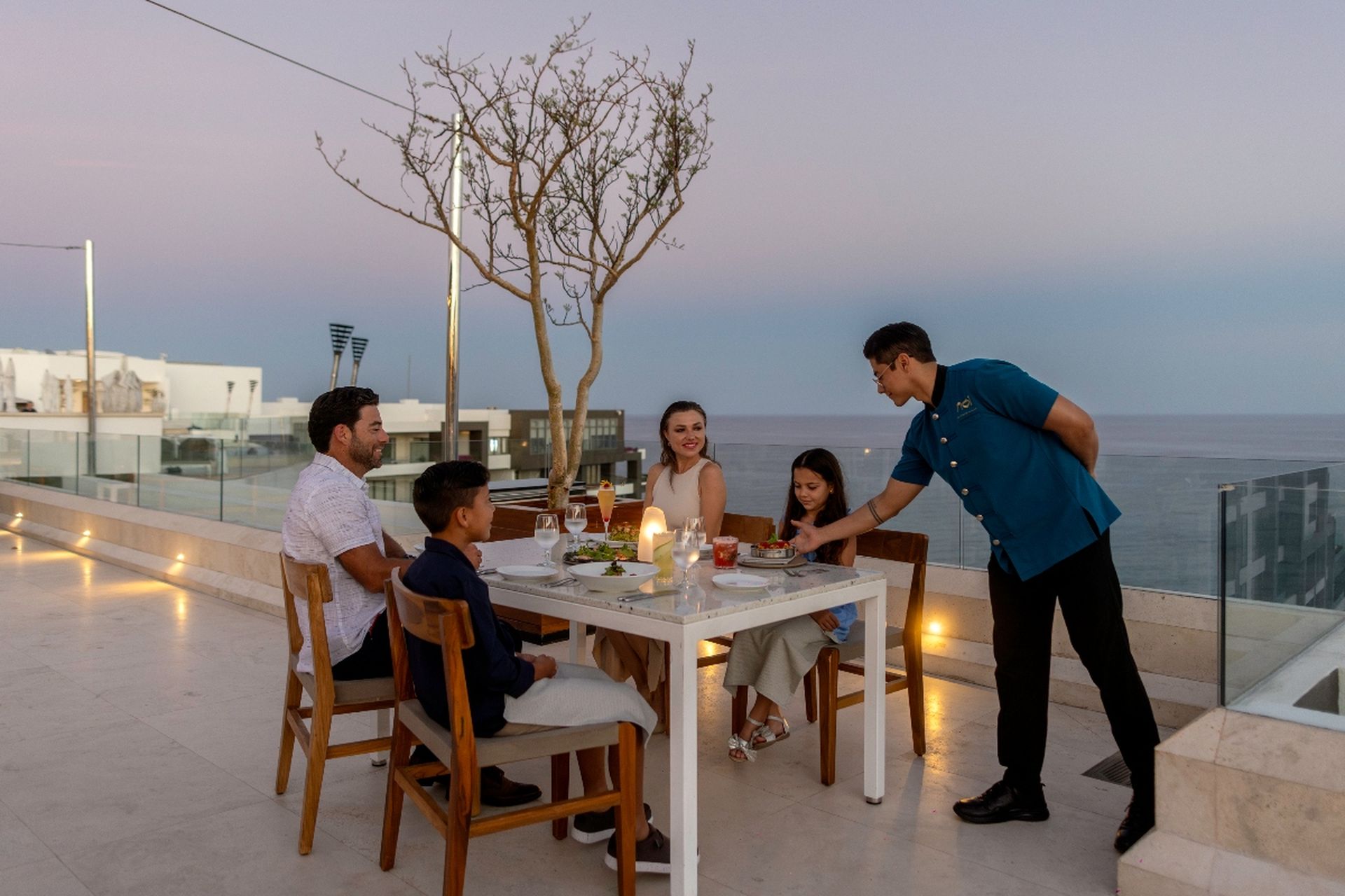 Family enjoying a gourmet rooftop dinner at Garza Blanca Cabo oceanfront terrace at sunset