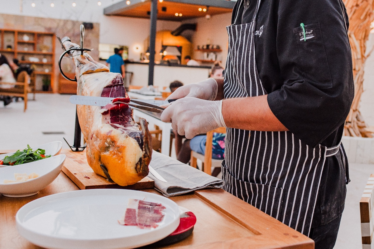 Chef carving jam&oacute;n at Garza Blanca Cabo, thin cured-ham slices plated beside salad