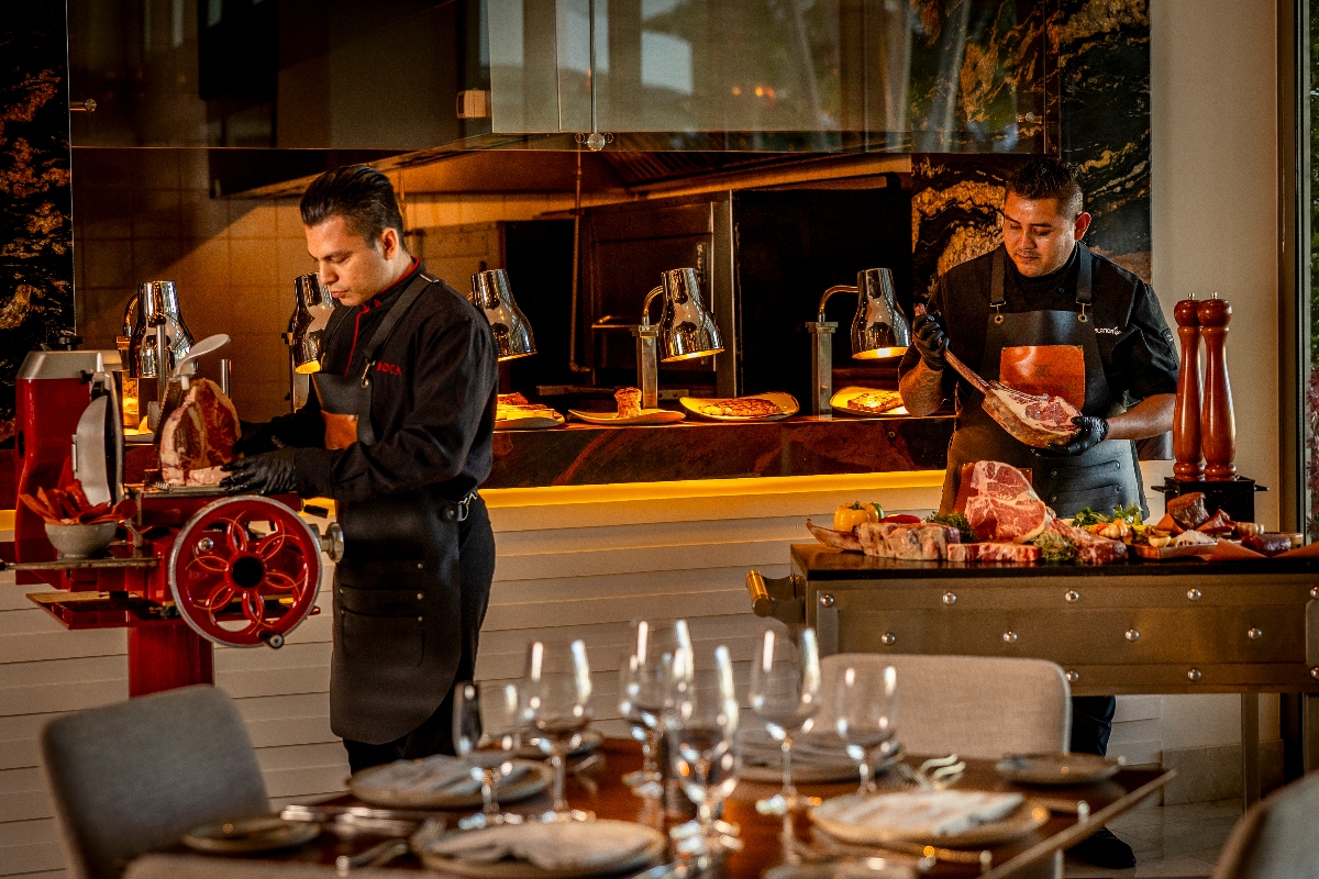 two meat sommeliers carving dry-aged steaks at an elegant carving station beside a set dining table