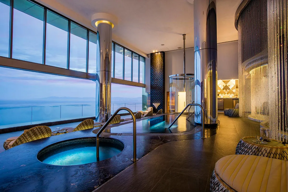 Luxurious indoor spa with whirlpools and panoramic ocean views at sunset, featuring elegant seating and ambient lighting.