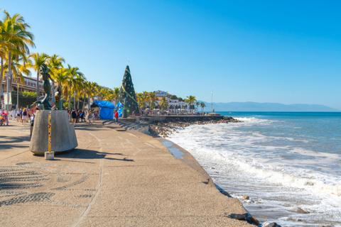 Beachfront promenade with palm trees, festive decorations, and gentle waves under a bright blue sky.