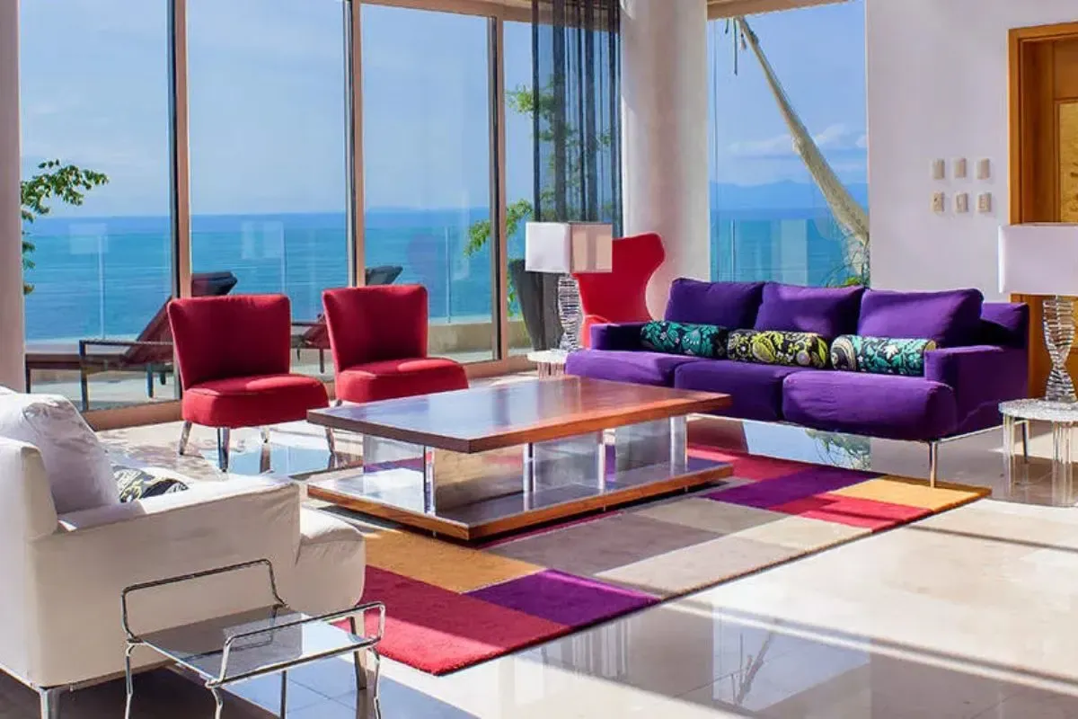 Luxurious beachfront living room with colorful seating, modern decor, and expansive ocean views through floor-to-ceiling windows.