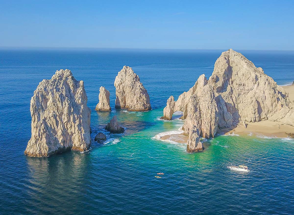 Stunning aerial view of rock formations rising from turquoise ocean waters at Land's End, Cabo San Lucas, under a clear blue sky.