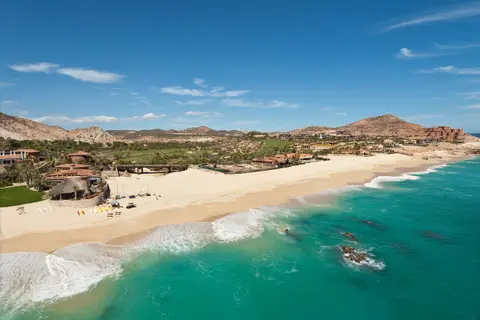 A luxurious Mexican beach resort along a pristine turquoise coastline; white sand, sun loungers, palms, and hillside villas.