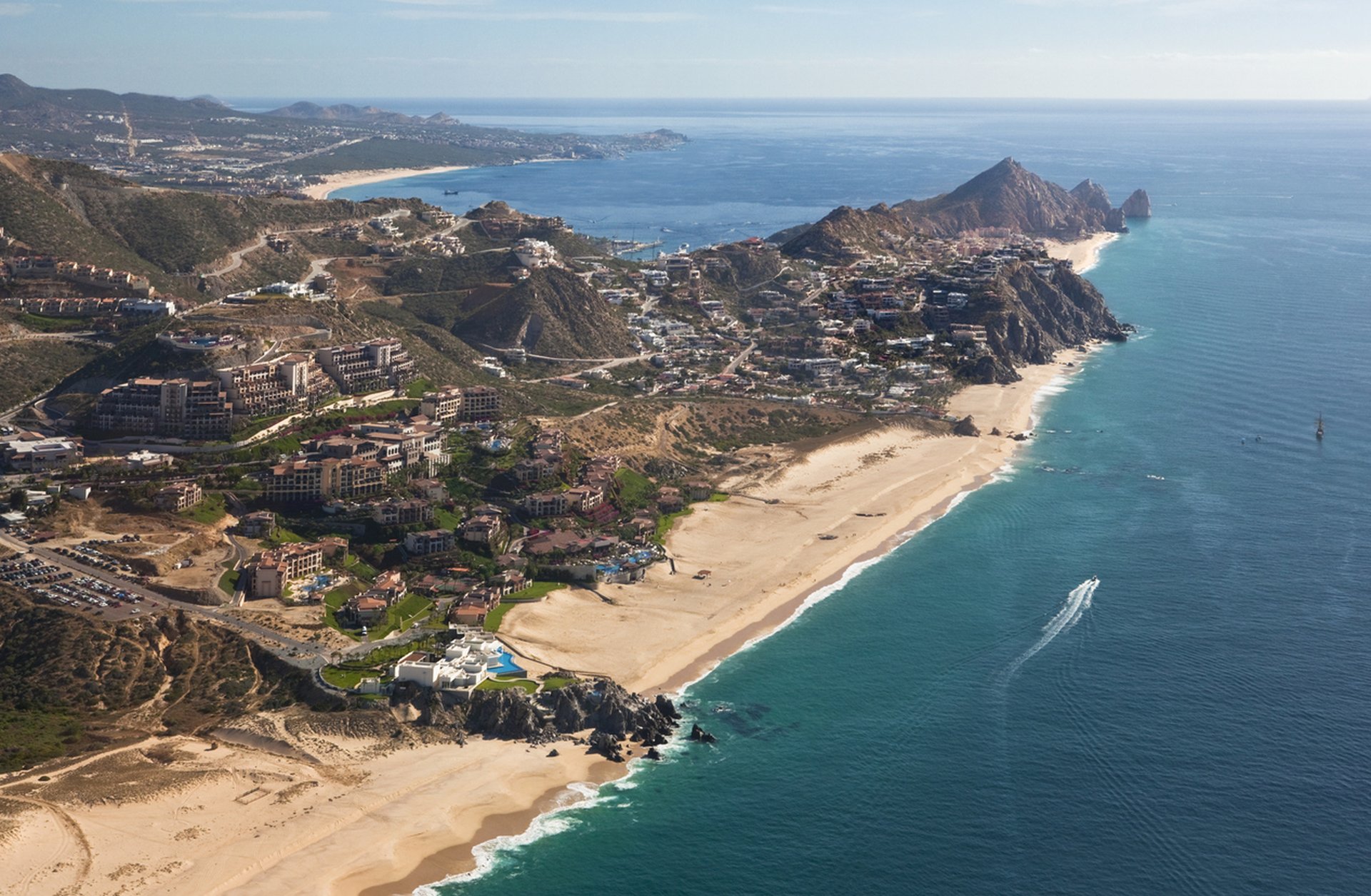 Aerial view of a luxury Mexico beach resort: golden sands, turquoise Pacific, cliffside villas, and hillside residences.