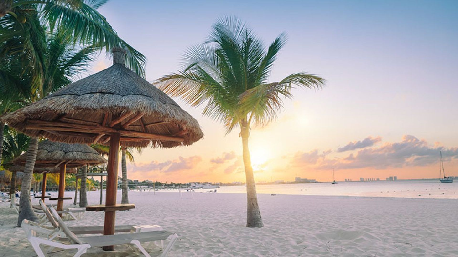 playa mujeres at sunrise with palm trees and thatched umbrellas, soft sand, and calm sea in the background.