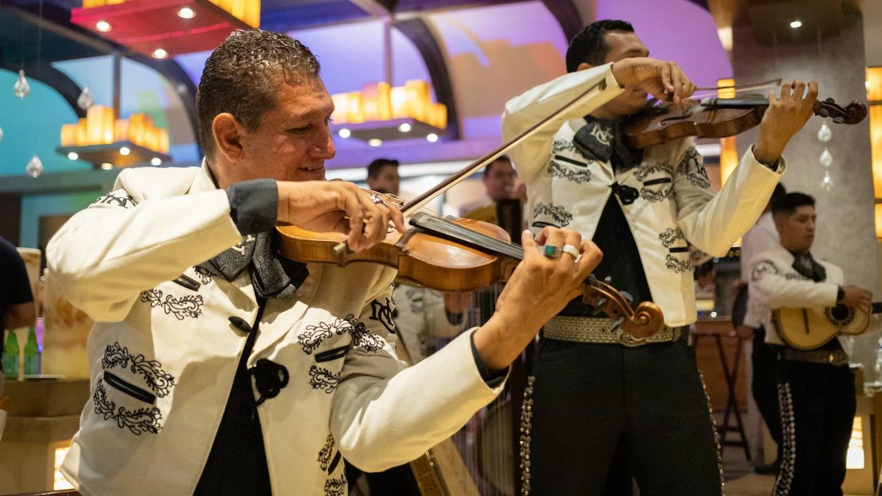 Mariachi band performs with violins in a vibrant setting, wearing traditional embroidered suits, creating a lively and cultural atmosphere.