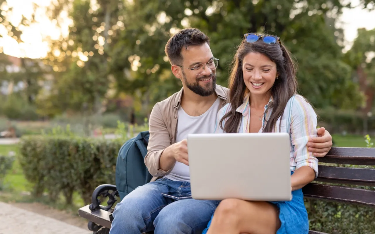 smiling-duo-checks-laptop-amidst-lush-park-setting-on-bench