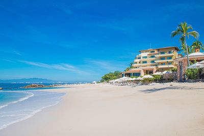 Garza Blanca luxury beachfront resort in México: white-sand beach, turquoise sea, palm trees, and sun loungers beneath white umbrellas.