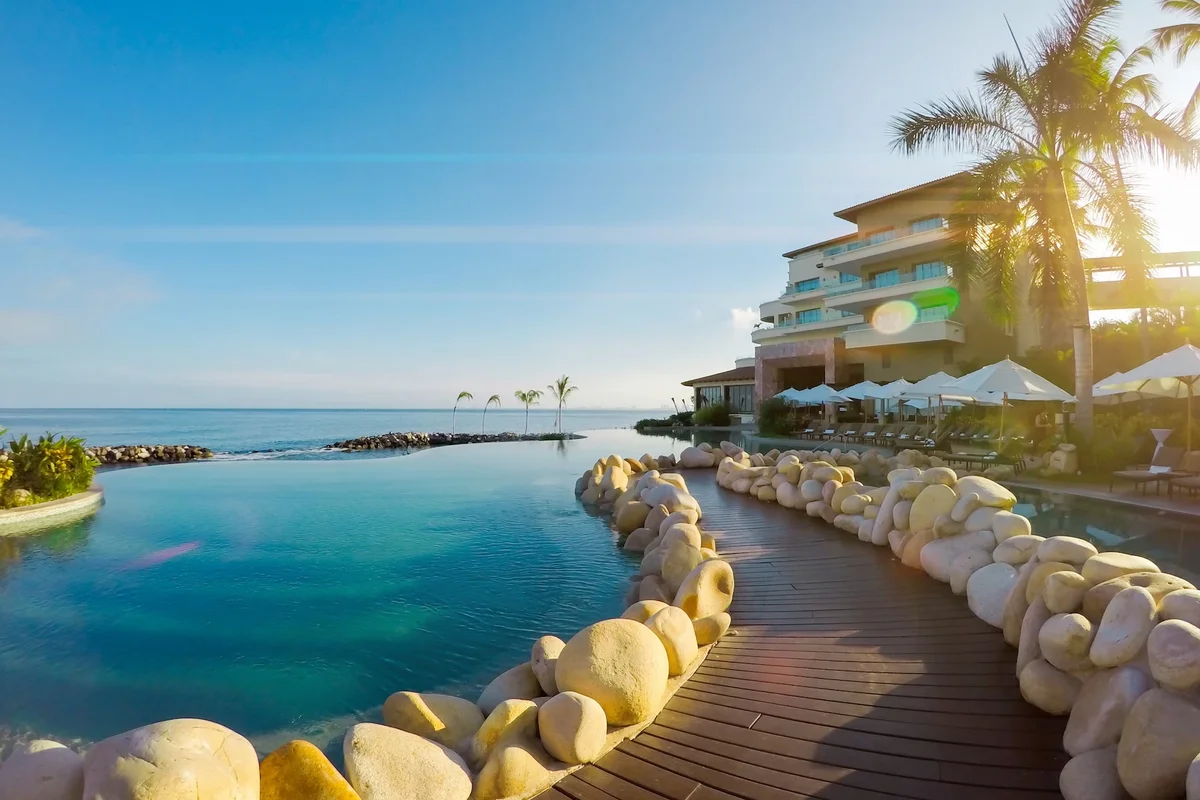 Oceanfront infinity pool lined with smooth boulders and a wooden deck at Garza Blanca Puerto Vallarta