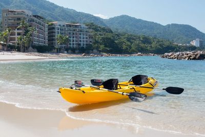 Bright yellow double kayak on Garza Blanca’s sandy beach, turquoise water, palm trees, and upscale resort buildings with green hills behind.