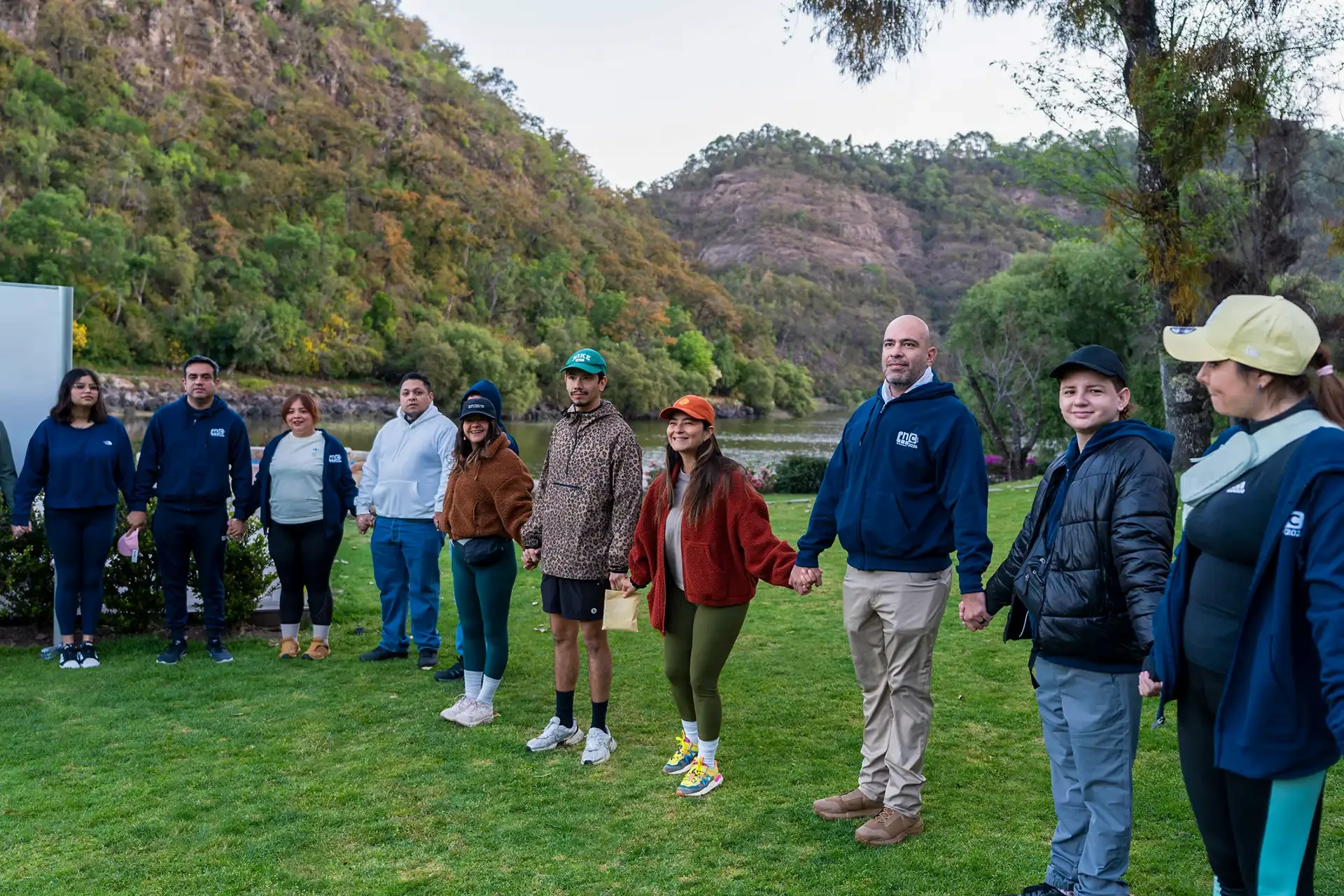 Group holding hands during a team building activity on the lakeside lawn at Sierra Lago