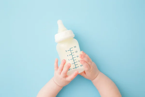 Baby holding a milk bottle with both hands on a light blue background.