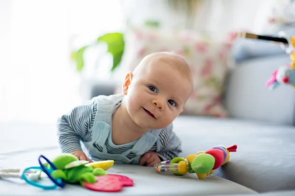 Baby smiling while lying on their stomach, surrounded by soft, colorful toys in a cozy room.