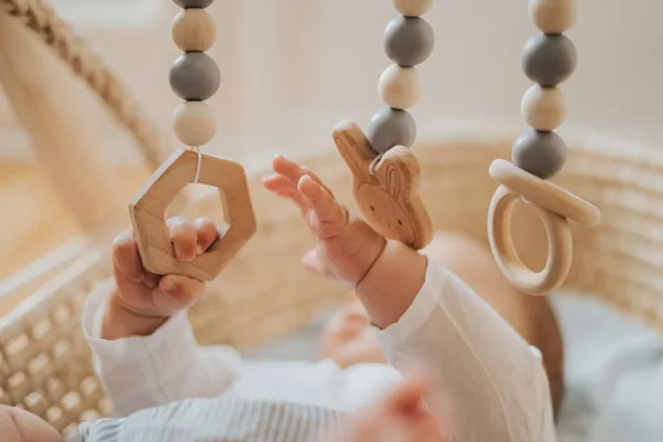 Baby reaching towards wooden hanging toys with geometric shapes in a crib.