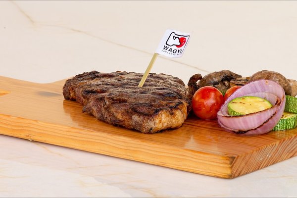 Grilled steak on a wooden board with zucchini, onion, mushroom, and tomato, garnished with a small flag.