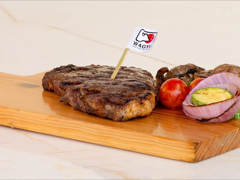 Grilled steak on a wooden board with zucchini, onion, mushroom, and tomato, garnished with a small flag.