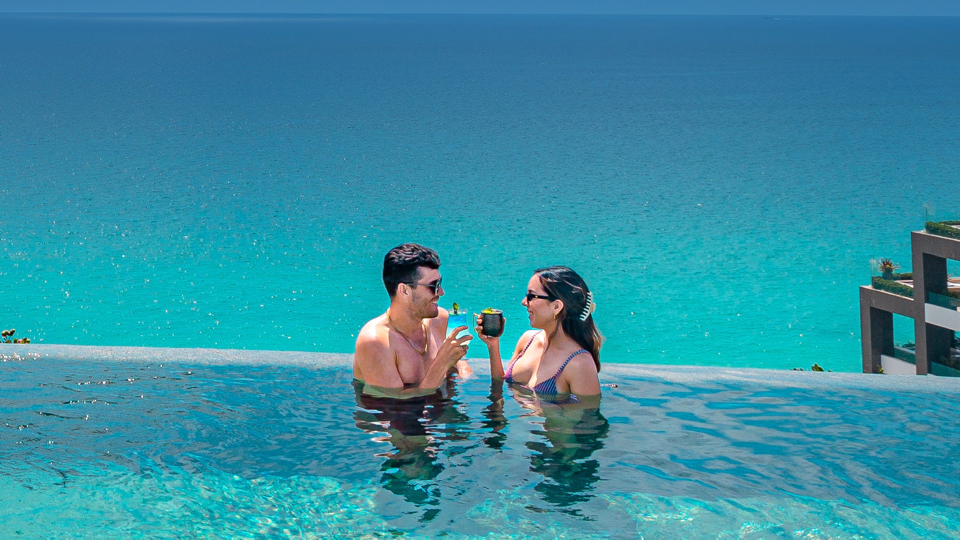 Couple toasts cocktails in an infinity pool at Garza Blanca, turquoise Caribbean waters to the horizon. Escape to the Extraordinary.