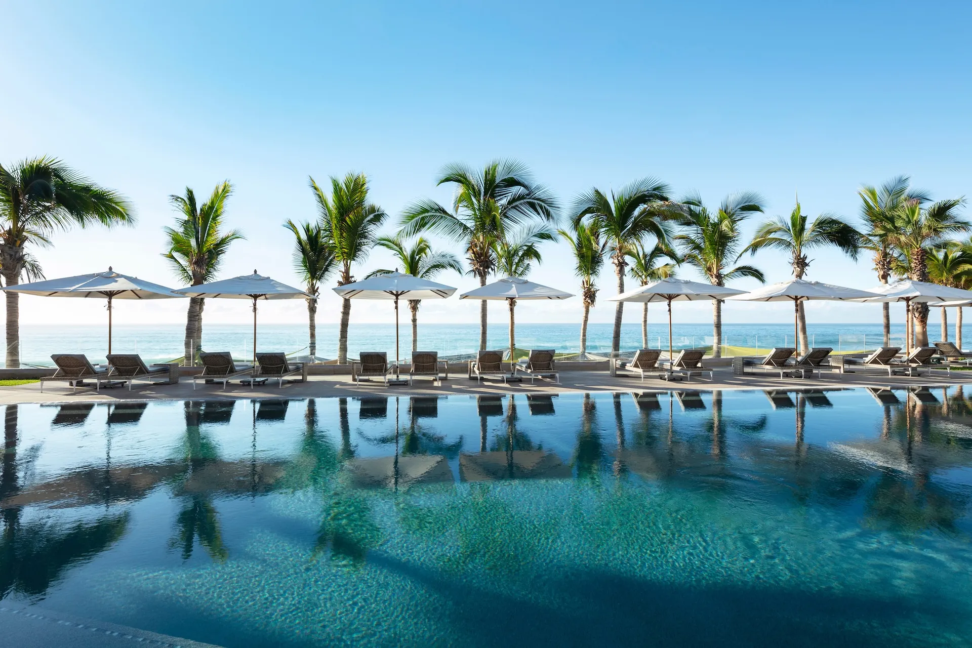 Garza Blanca Los Cabos: infinity pool with sun loungers and umbrellas, palms overlooking turquoise Caribbean, Escape to the Extraordinary.