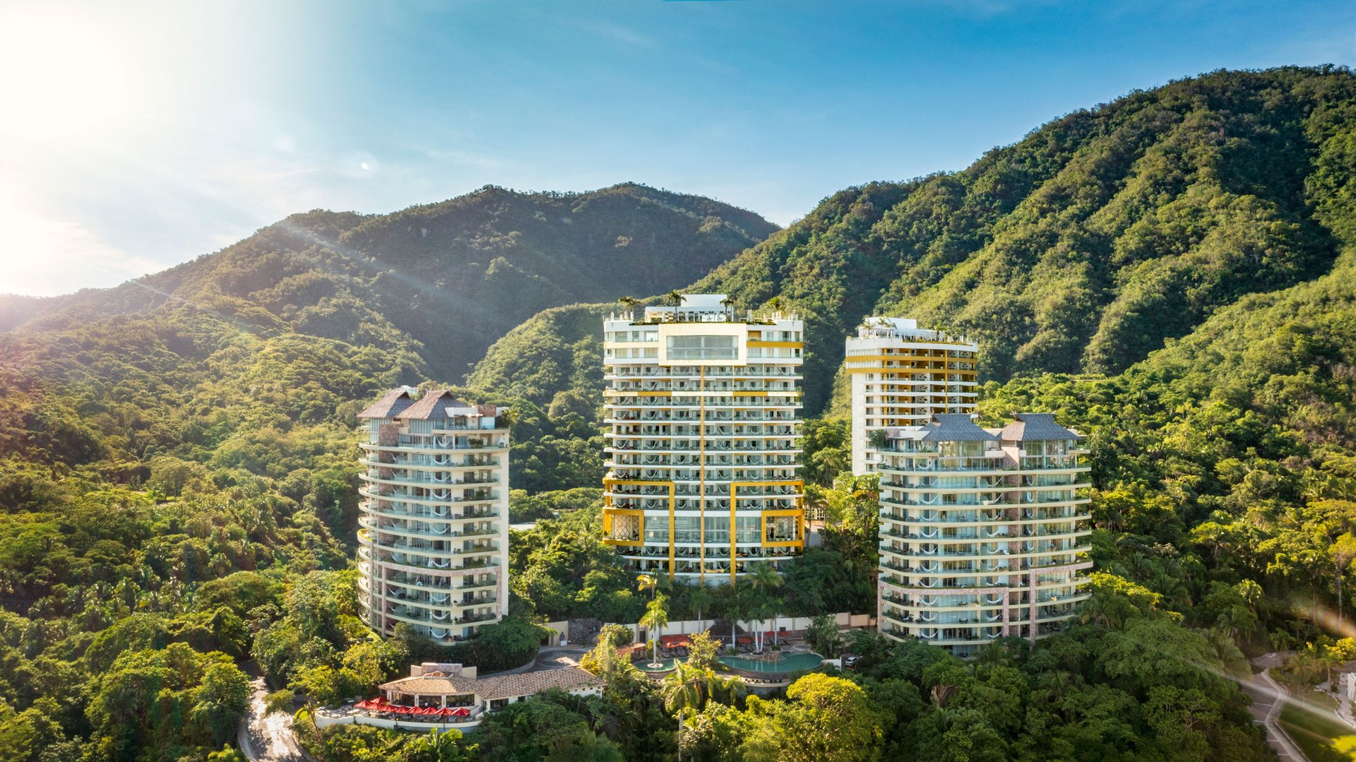 Aerial view of luxury resort towers nestled among lush green hills under a clear blue sky.