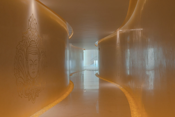 A dimly lit hallway with smooth, curved walls and a Buddha mural on the left. The floor is glossy, reflecting warm orange lighting.