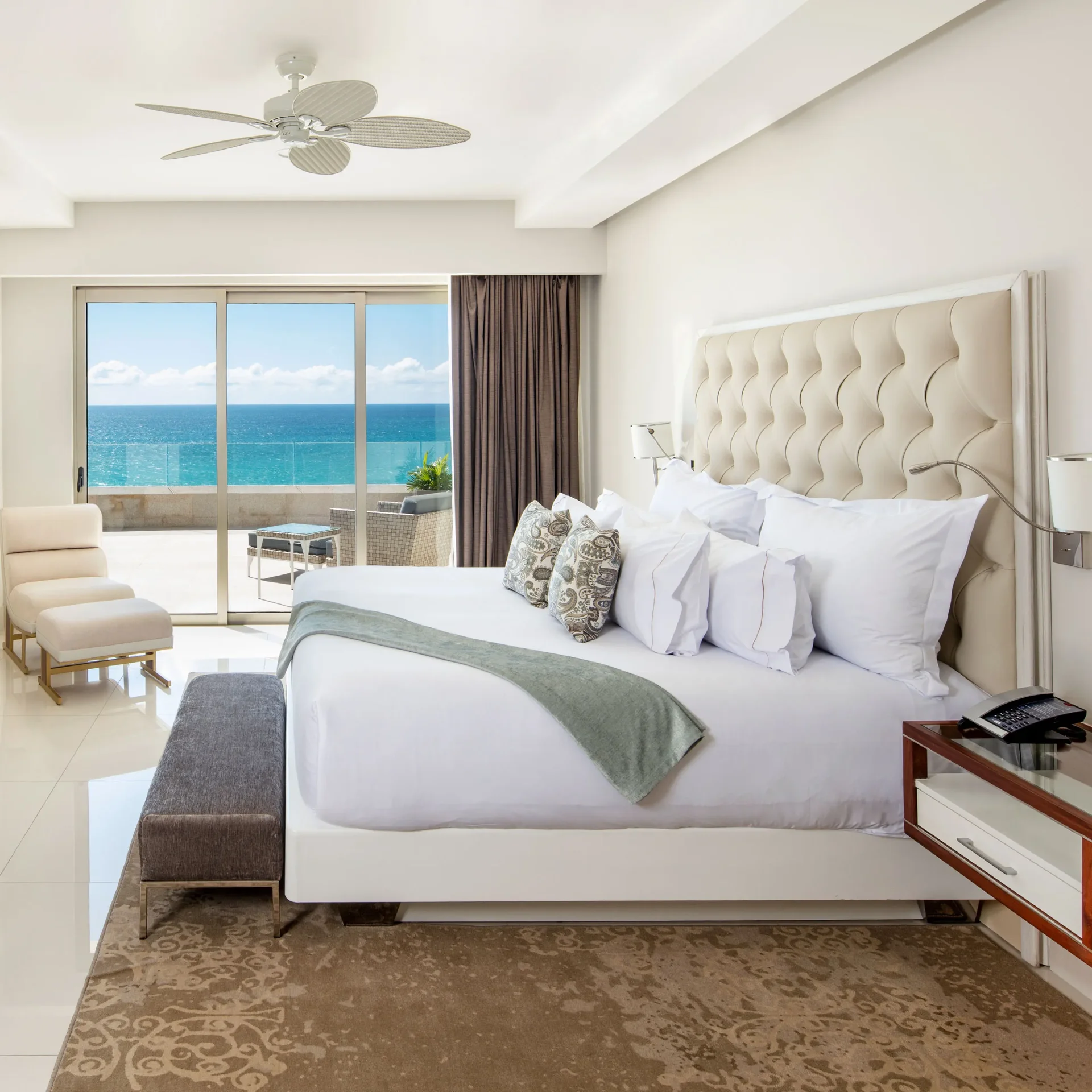 Luxurious Garza Blanca suite: king bed with tufted headboard, white linens, seating area, and balcony overlooking the turquoise sea.