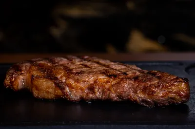 Grilled steak with char marks on a dark surface, showcasing a juicy, well-cooked texture.