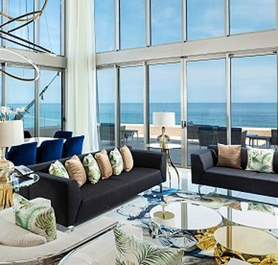 Luxurious living room with floor-to-ceiling windows, ocean view, modern sofas, tropical cushions, and elegant decor.