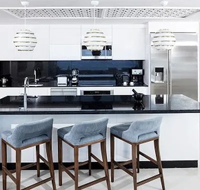 Modern kitchen with a black countertop, white cabinets, three pendant lights, and three blue cushioned bar stools. Stainless steel appliances.