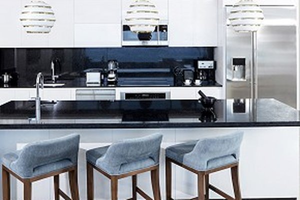 Modern kitchen with a black countertop, white cabinets, three pendant lights, and three blue cushioned bar stools. Stainless steel appliances.