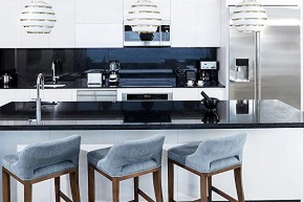 Modern kitchen with a black countertop, white cabinets, three pendant lights, and three blue cushioned bar stools. Stainless steel appliances.