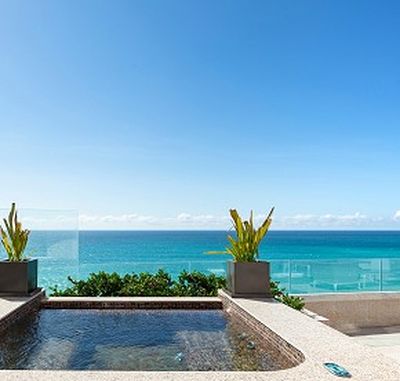 Rooftop pool with clear blue ocean view, flanked by potted plants under a bright, cloudless sky.