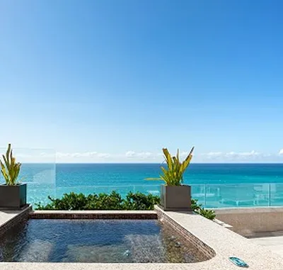 Rooftop pool with clear blue ocean view, flanked by potted plants under a bright, cloudless sky.