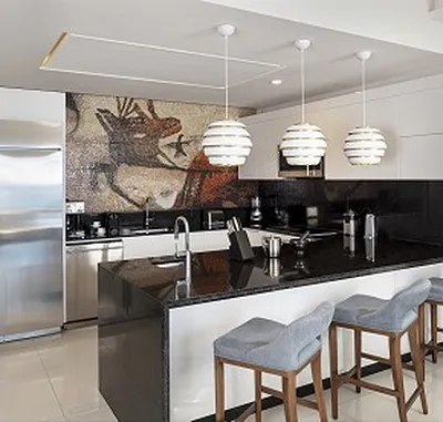 Modern kitchen with a black granite countertop, three pendant lights, bar stools, stainless steel appliances, and a mosaic wall mural.