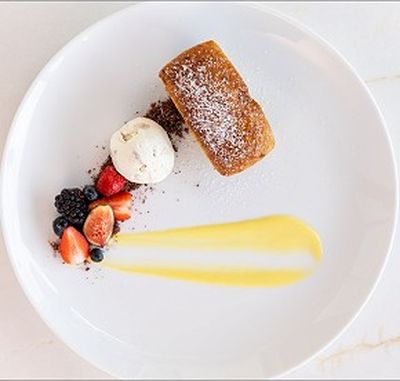 Dessert plate with a slice of cake, vanilla ice cream, mixed berries, and a swipe of yellow sauce on a white background.