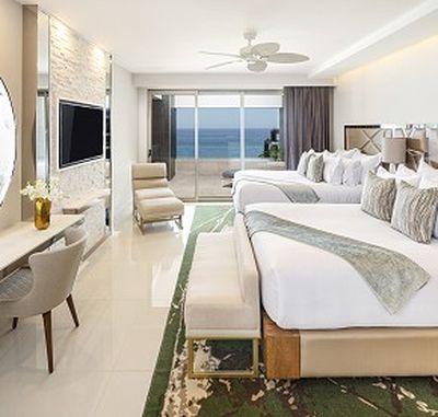 Modern hotel room with two beds, a TV, desk, and seating area. Large window with ocean view. Neutral tones and elegant decor.