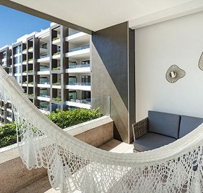 Balcony with a white hammock, gray sofa, and view of modern apartment buildings under a clear blue sky.