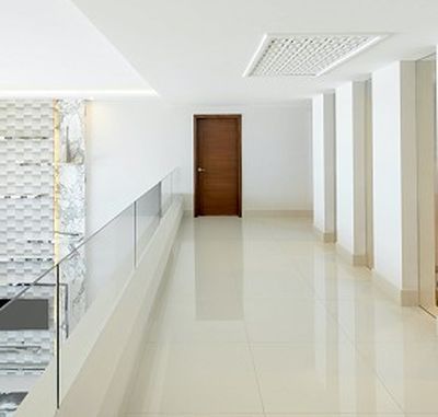 Minimalist hallway with glossy white floors, a wooden door at the end, glass railing on the left, and recessed lighting on the ceiling.