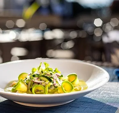 A white plate with a fresh salad, garnished with sliced cucumbers, red onions, and herbs, on a blurred background.
