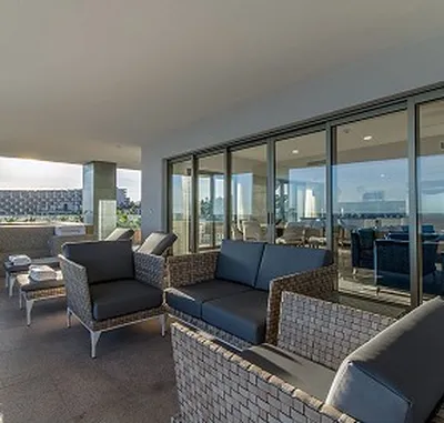 Outdoor patio with wicker furniture, gray cushions, and glass doors. Overlooks a scenic view with buildings in the distance.