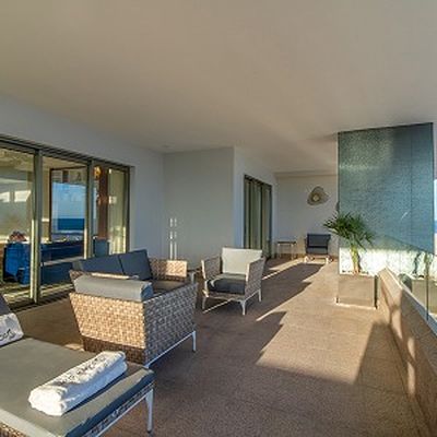 Spacious outdoor patio with wicker furniture, cushioned seating, and potted plants, bathed in natural sunlight.