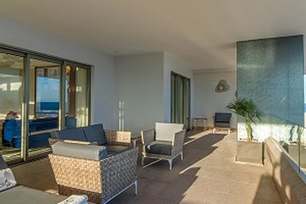 Spacious outdoor patio with wicker furniture, cushioned seating, and potted plants, bathed in natural sunlight.