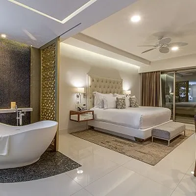 Luxurious hotel room with a king-size bed, modern decor, freestanding bathtub, ceiling fan, and large mirror reflecting the elegant space.
