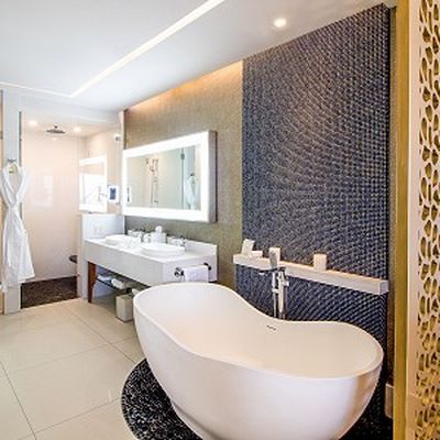 Modern bathroom with a freestanding white bathtub, double sink vanity, illuminated mirror, and textured wall tiles, featuring a sleek, minimalist design.
