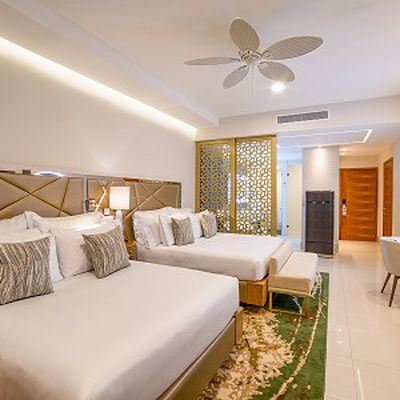 Elegant hotel room with two double beds, decorative pillows, a ceiling fan, wooden accents, and a patterned room divider.