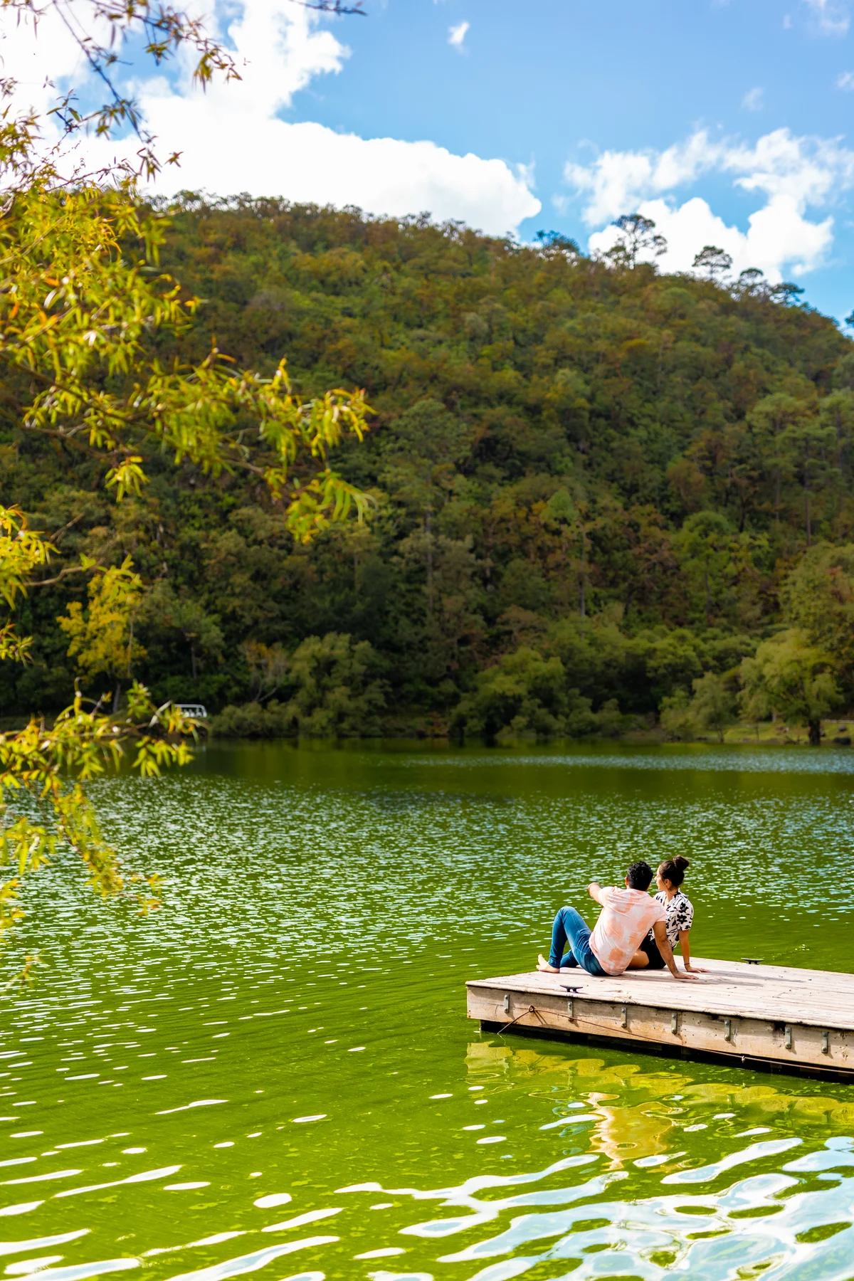 Pareja sentada en el muelle sobre las aguas verdes de la laguna